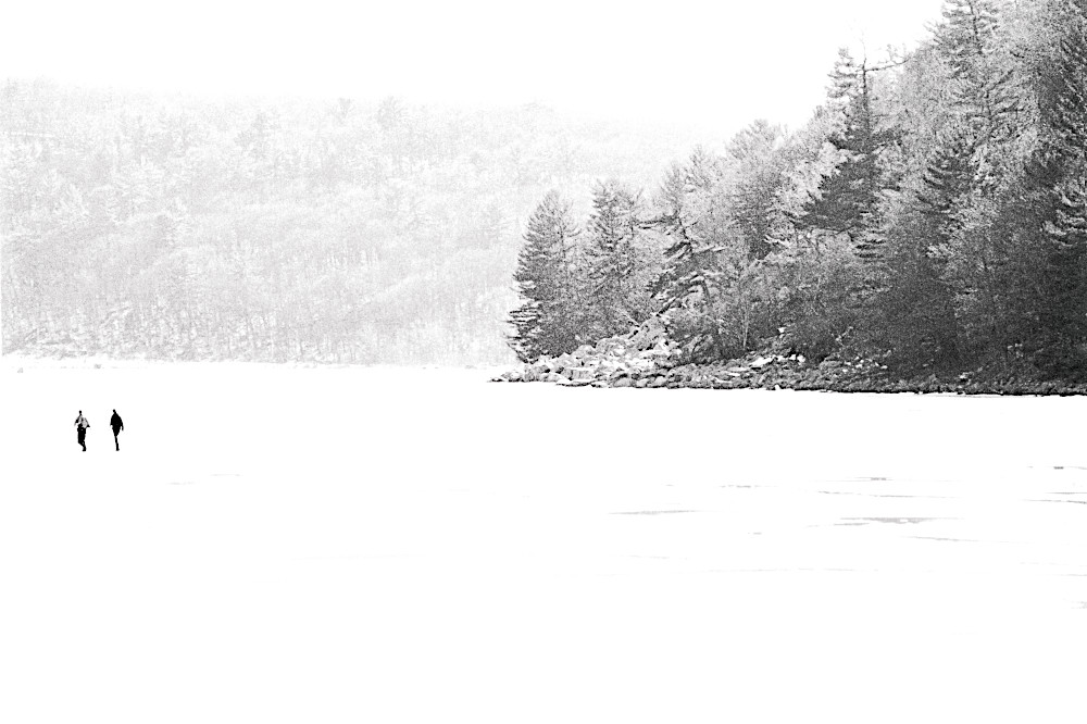 A stark monochrome of two figures walking on a frozen lake.