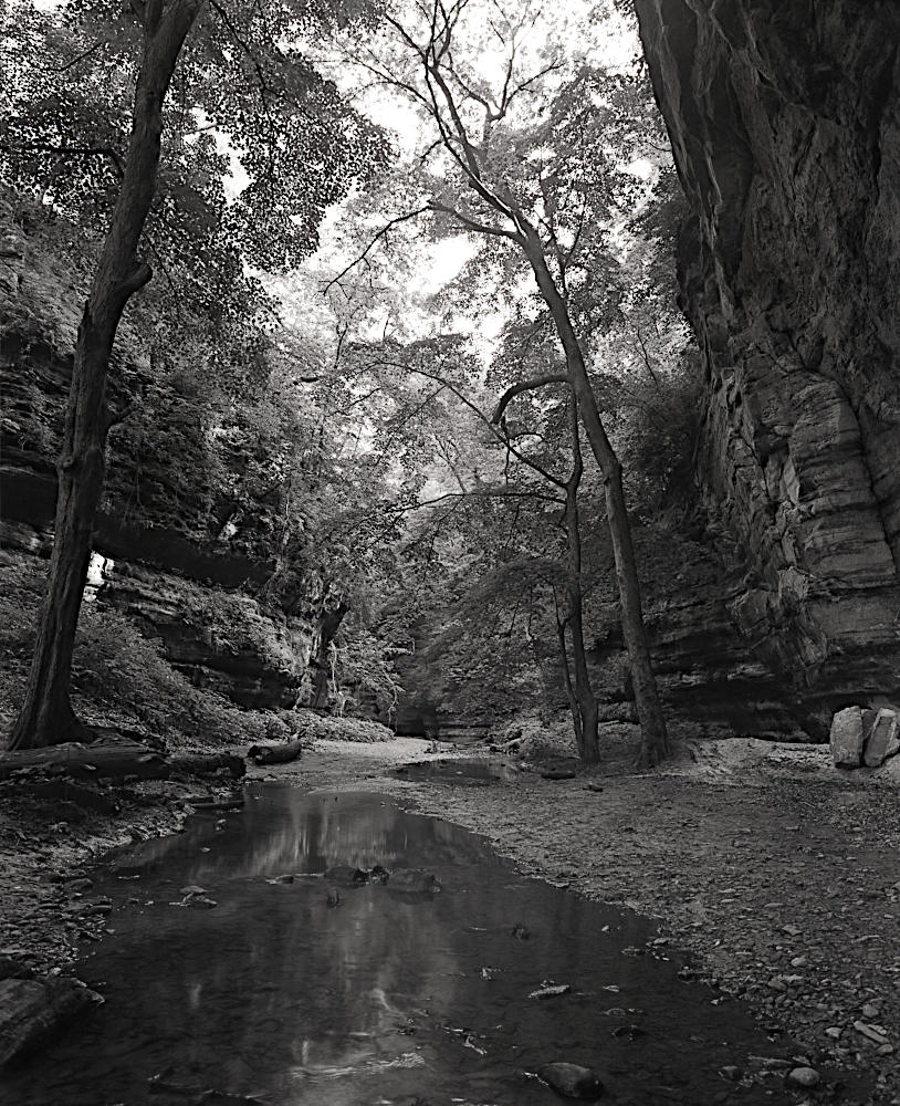 A dramatic monochrome of a stream running between two large bluffs.