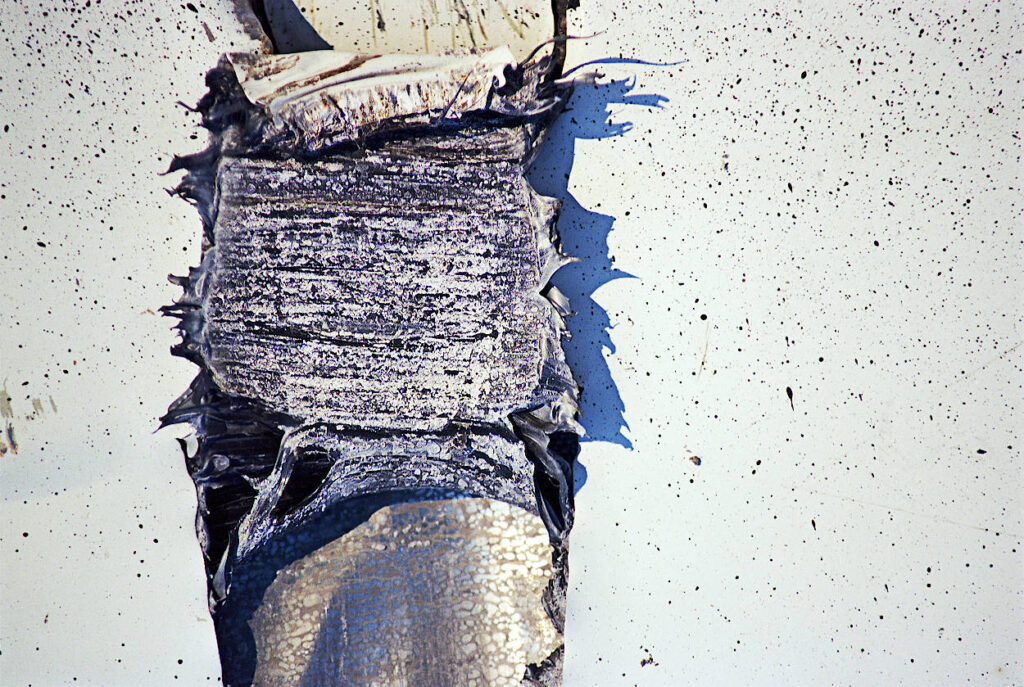 A gouge in a metal sign, seen as crop spoilage induced by climate change